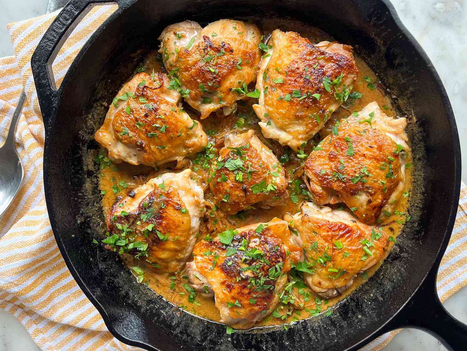 Cooked chicken thighs in a skillet topped with herbs