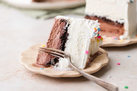 Slice of Ice Cream Cake on a Small Plate with a Fork with More Cake in the Background