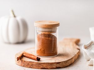 Homemade pumpkin pie spice blend in a jar on a wooden cutting board.