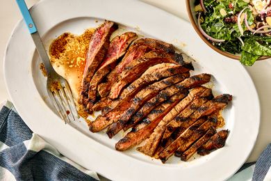 Sliced marinated flank steak on a serving platter with a fork on the side