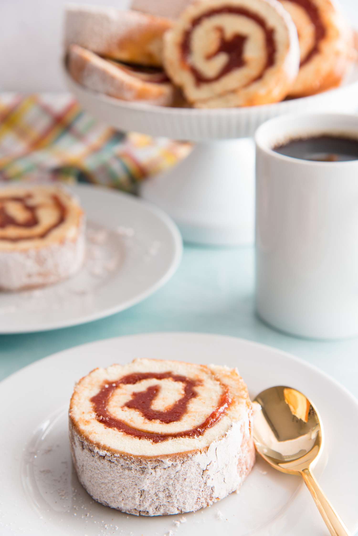 Guava Jelly Roll Cake on a plate with more slices set behind it on a cake stand.