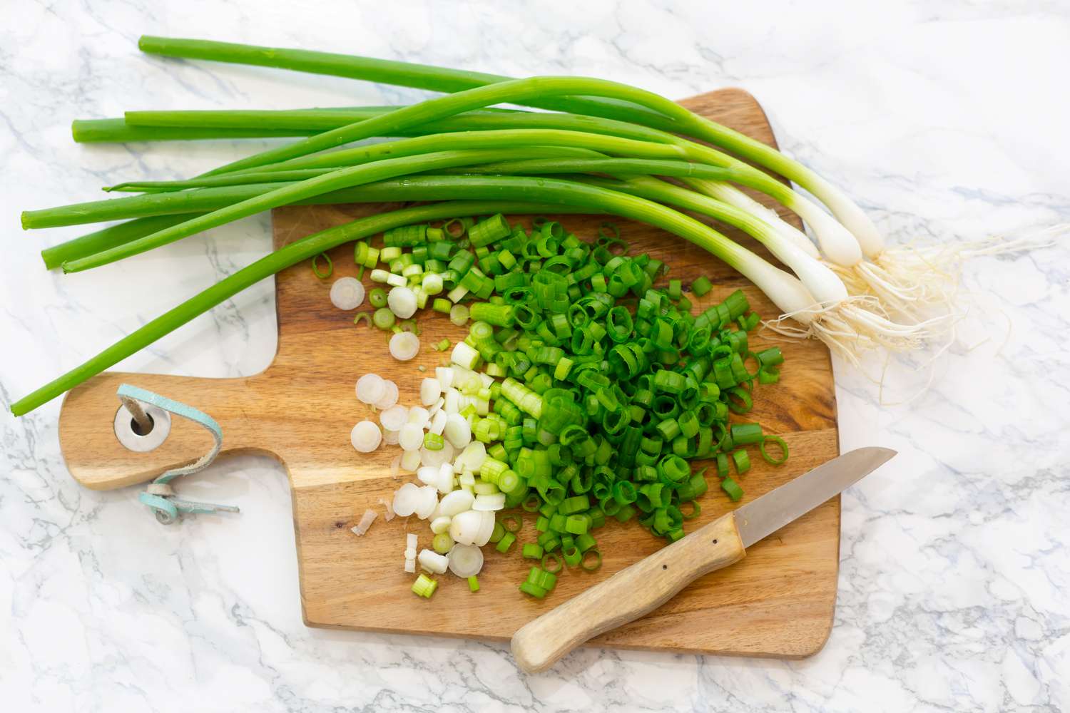 Overhead shot of a bunch of scallions, part of them chopped up, on a wooden cutting board