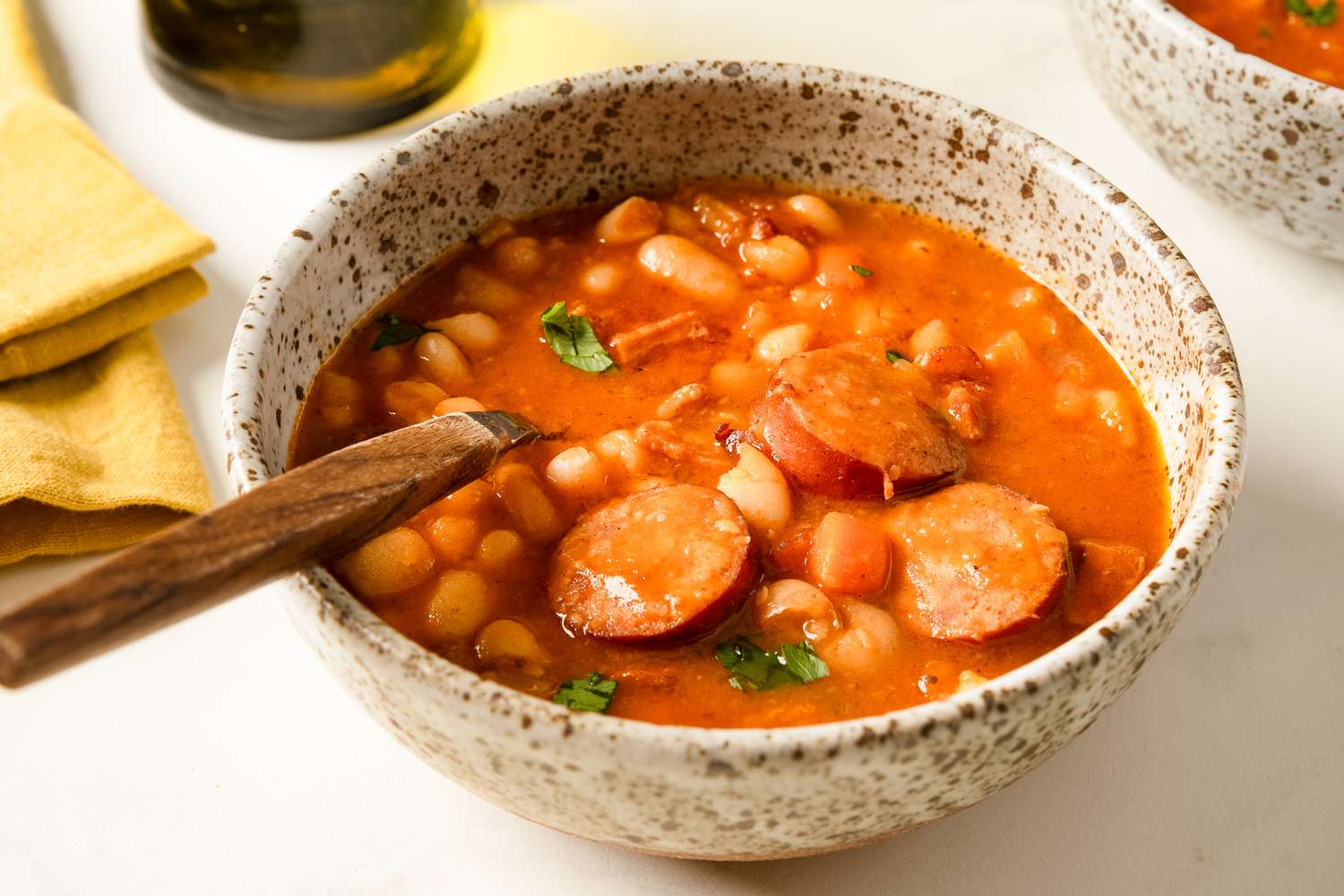 A bowl of bean soup with slices of sausage and a spoon