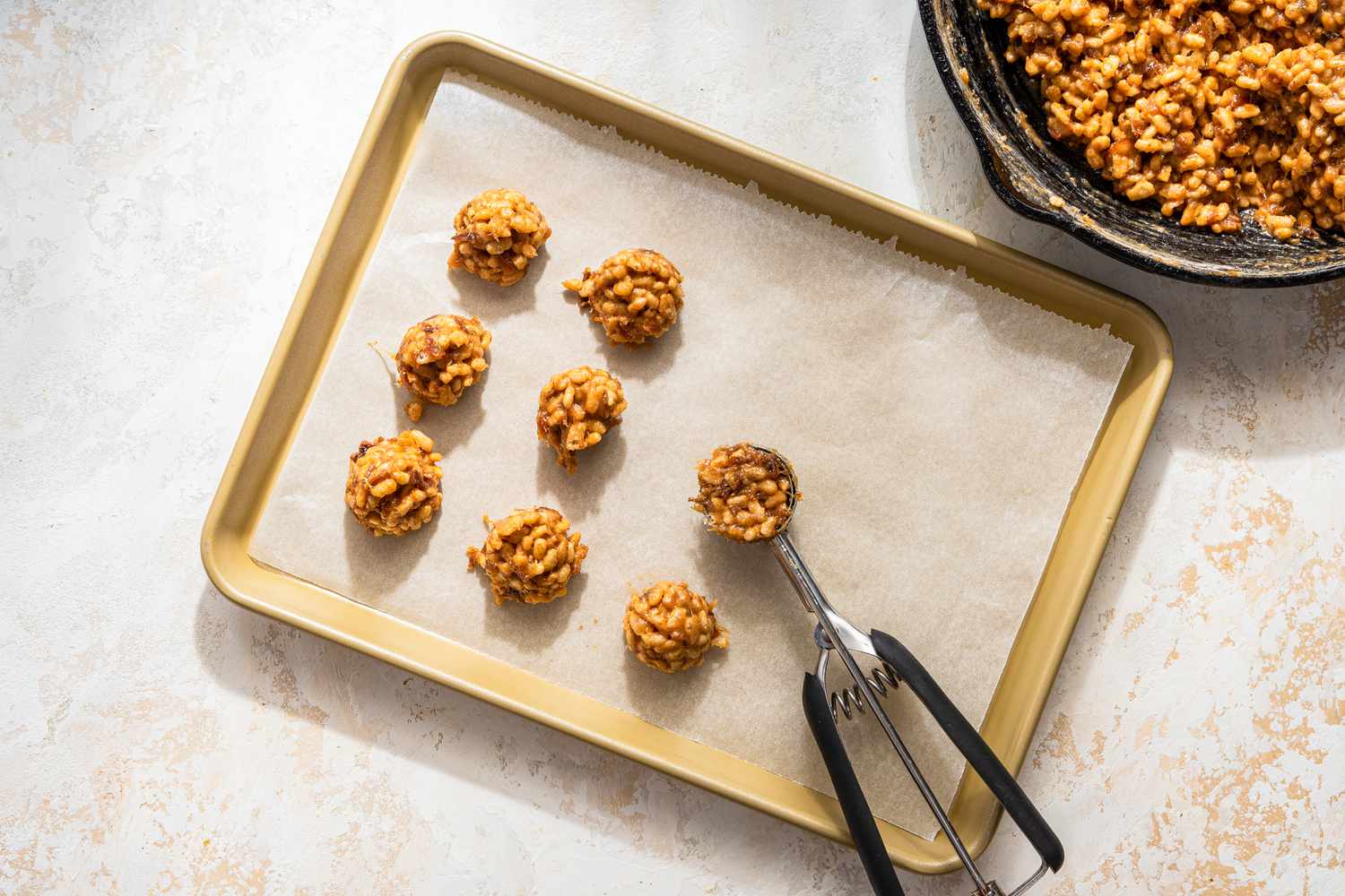Cookie scoop used to measuring out the date skillet cookies onto a parchment paper lined baking sheet