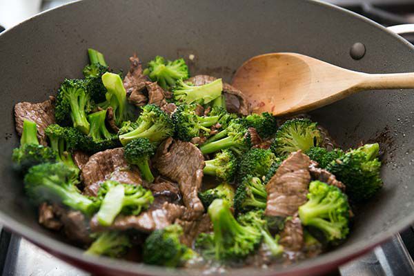 beef and broccoli in wok with wooden spoon