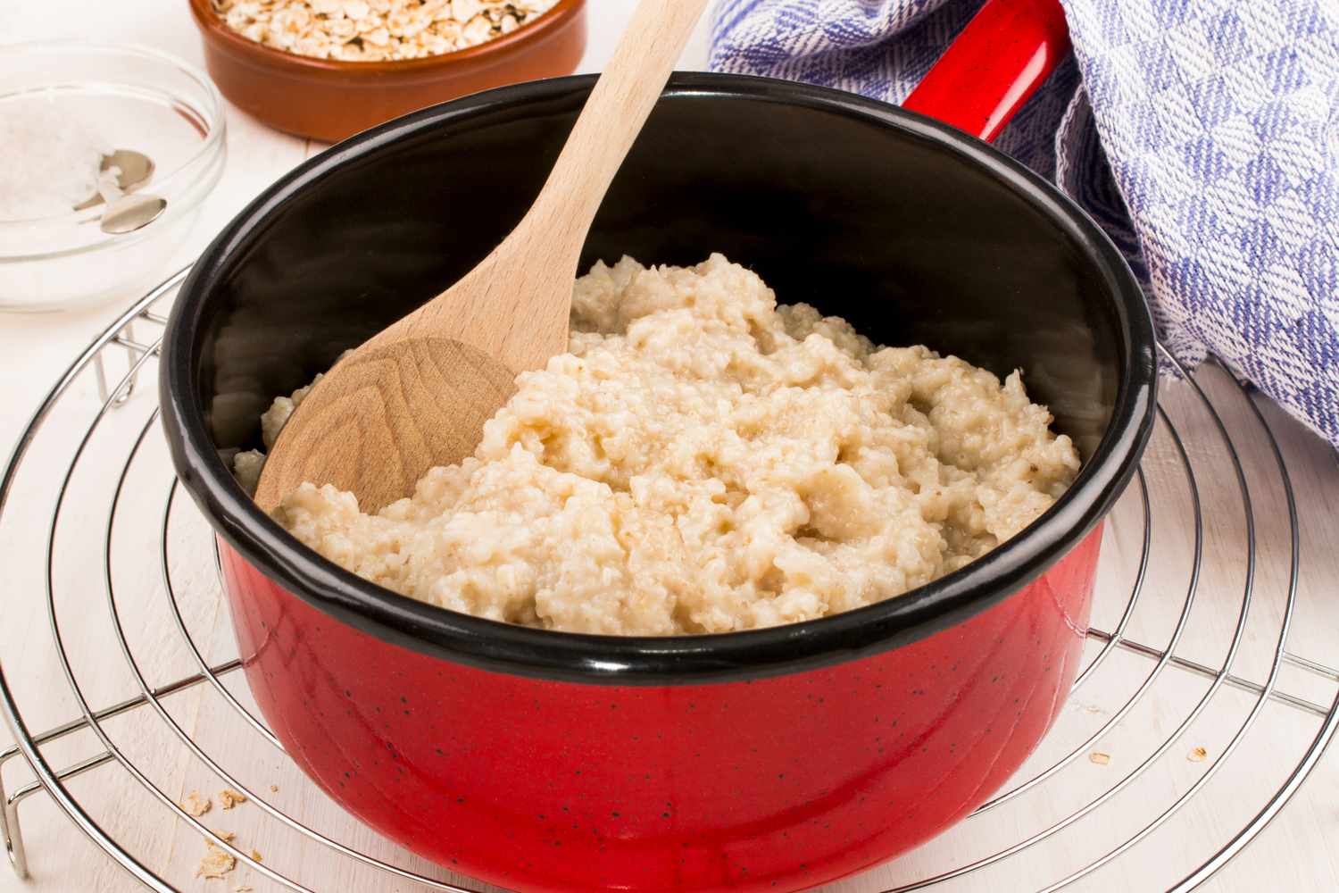 A red pot of oatmeal with a wooden spoon on a wire cooling rack
