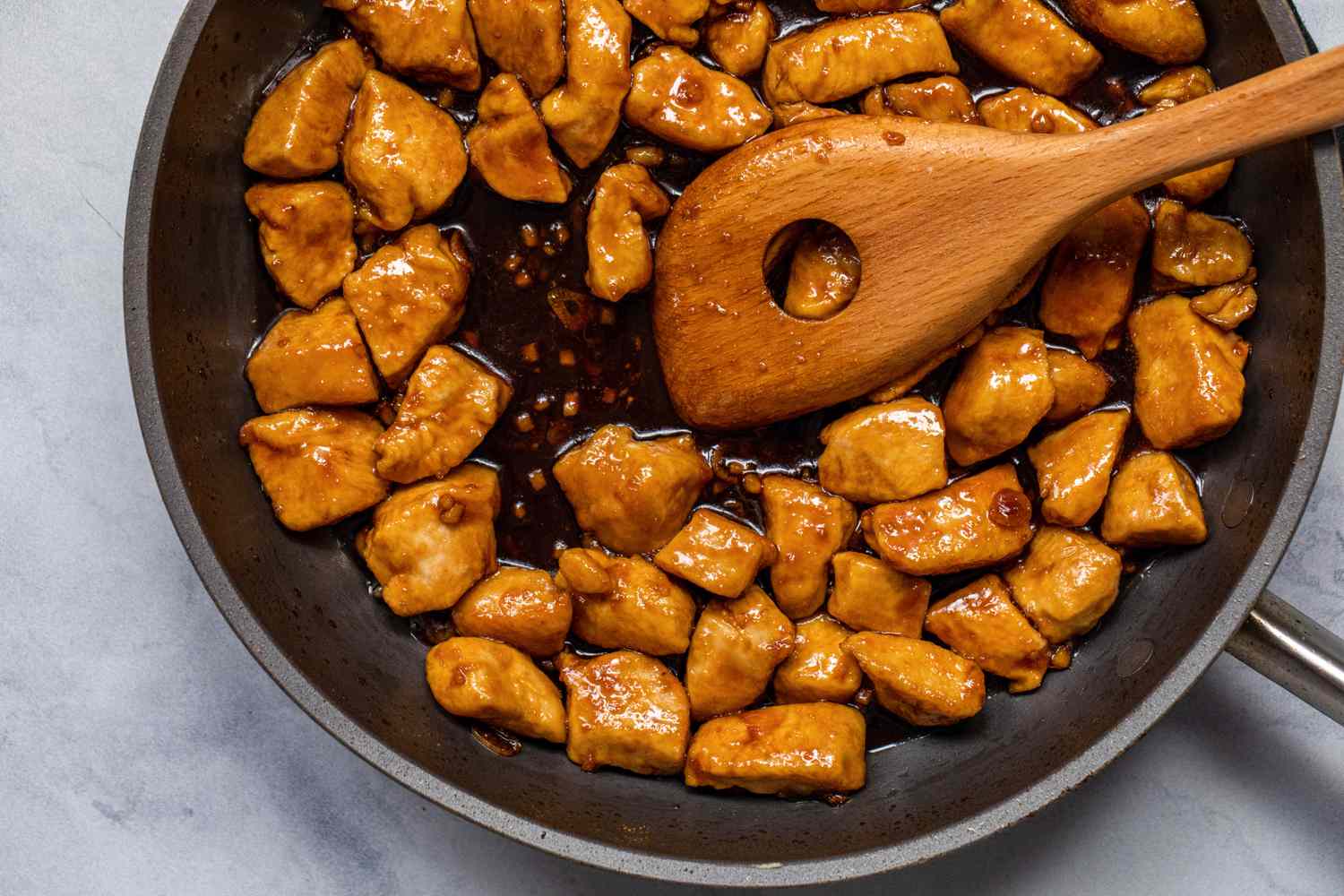 A wooden spoon stirring Sweet and Tangy Bourbon Chicken in a skillet.