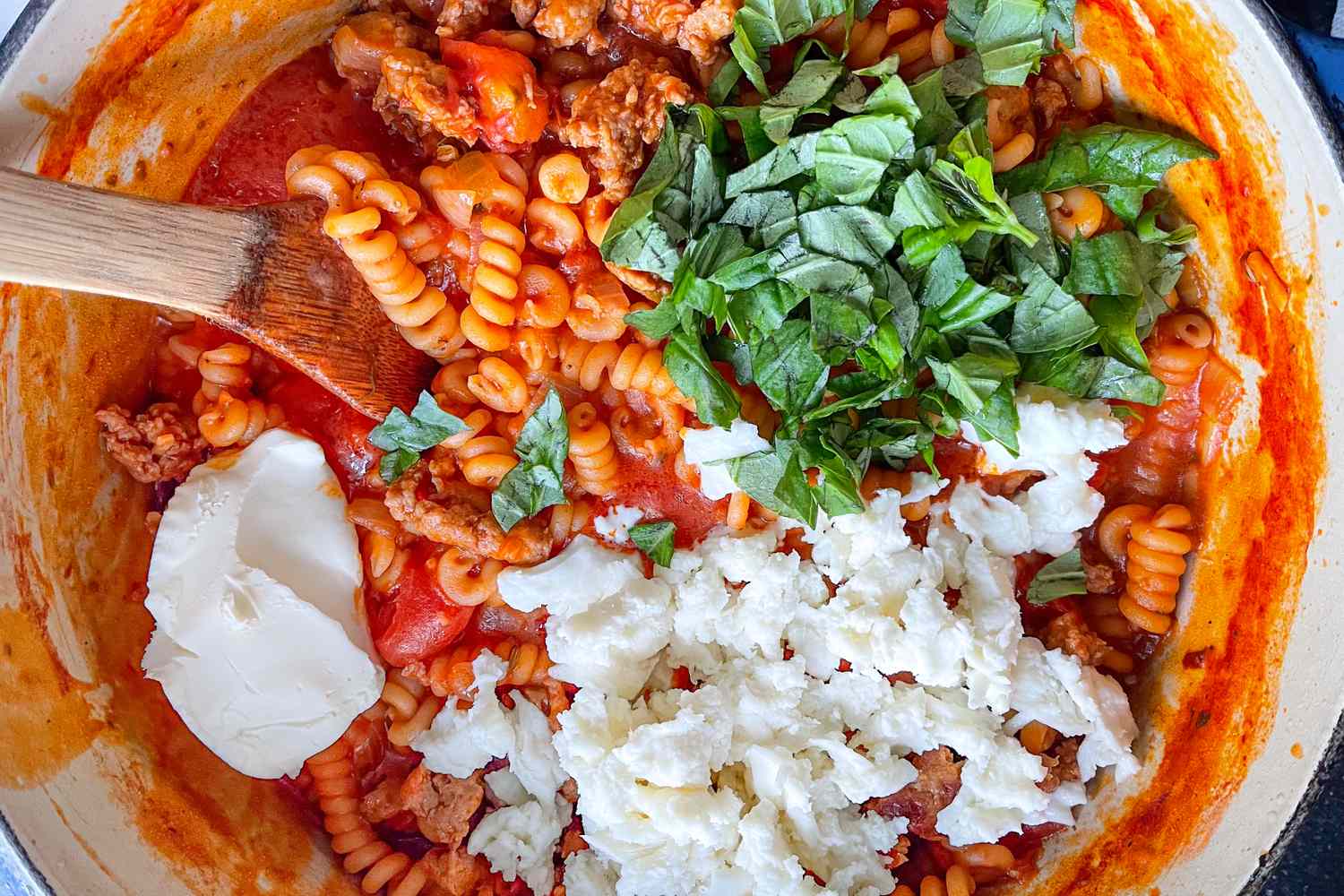 Pasta with tomato sauce fresh basil ricotta cheese and ground meat being mixed in a pot