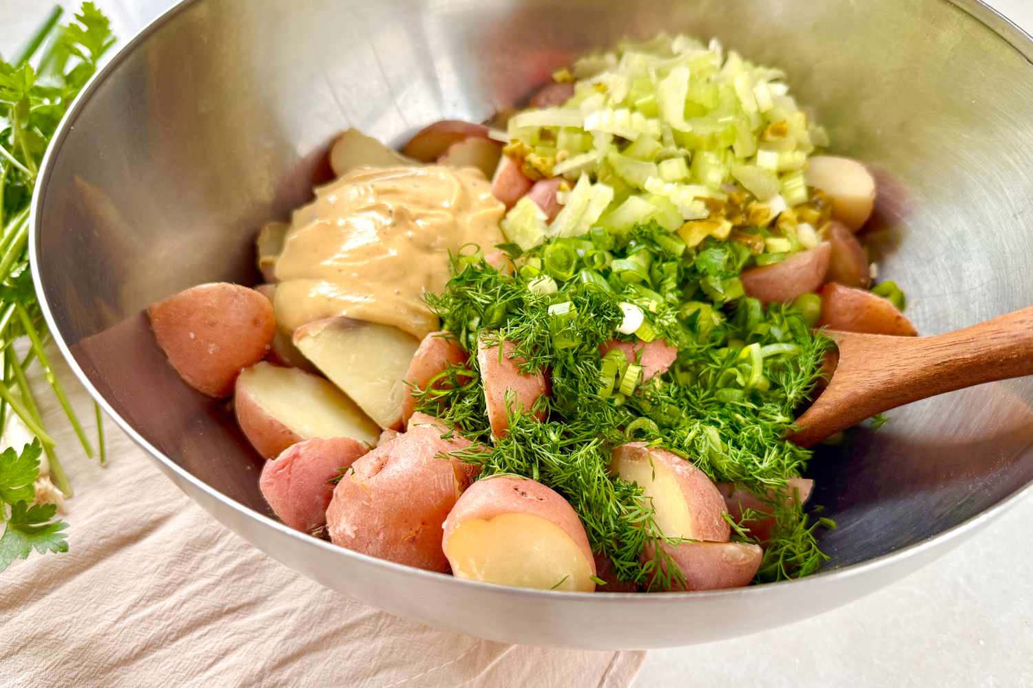 Ingredients for potato salad in a metal bowl with a wooden spoon