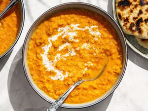 Coconut Lentil Soup garnished with yogurt in a bowl with a spoon, naan on the side
