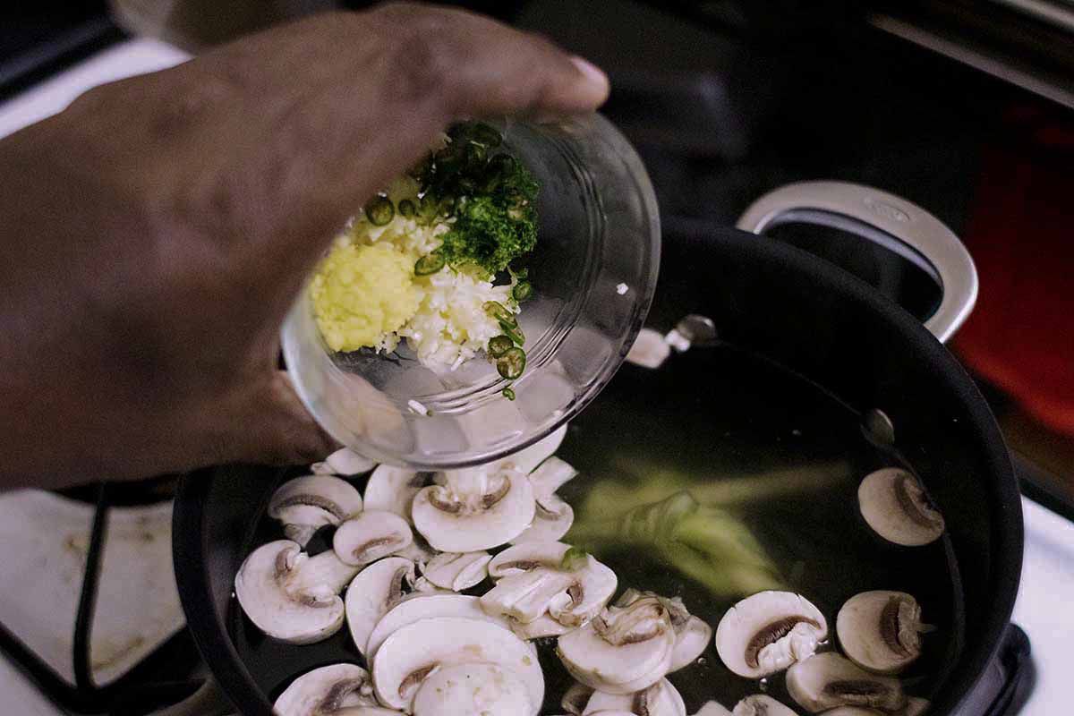Spices are being added to a black pot on the stove for thai style shrimp soup.