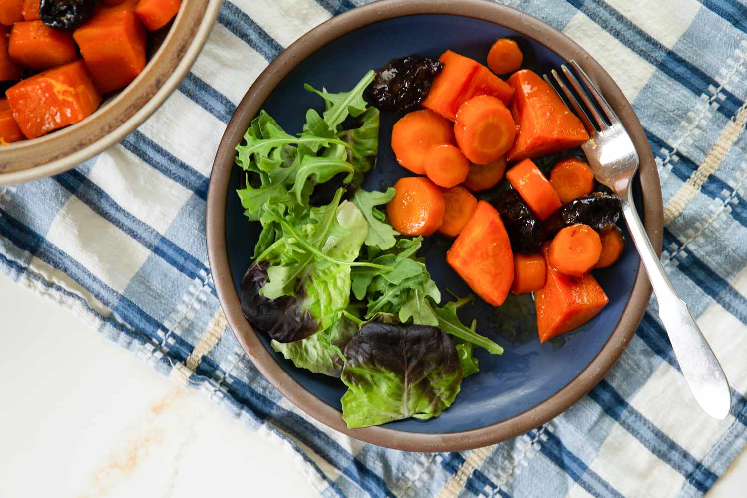 Carrot and Sweet Potato Tzimmes on a small plate with mixed greens and a fork