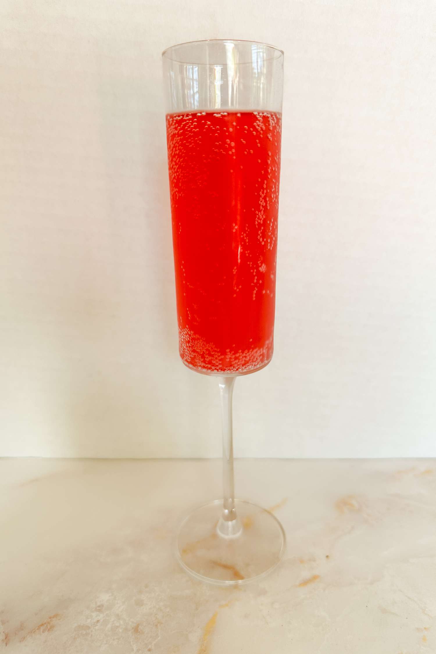 A glass filled with a pink bubbly drink on a white surface