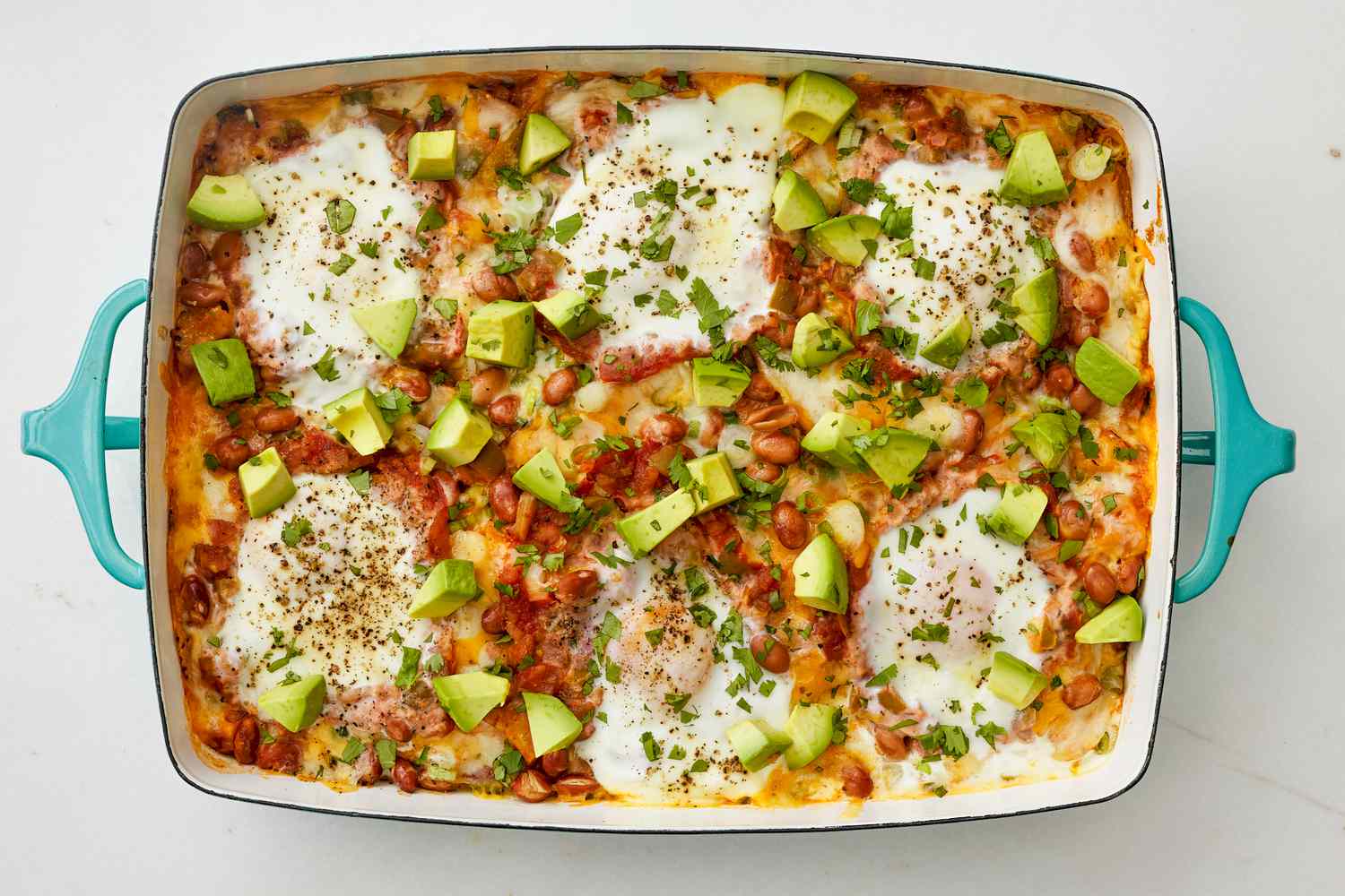Baked huevos rancheros casserole in a casserole dish topped with avocado cubes and minced herbs