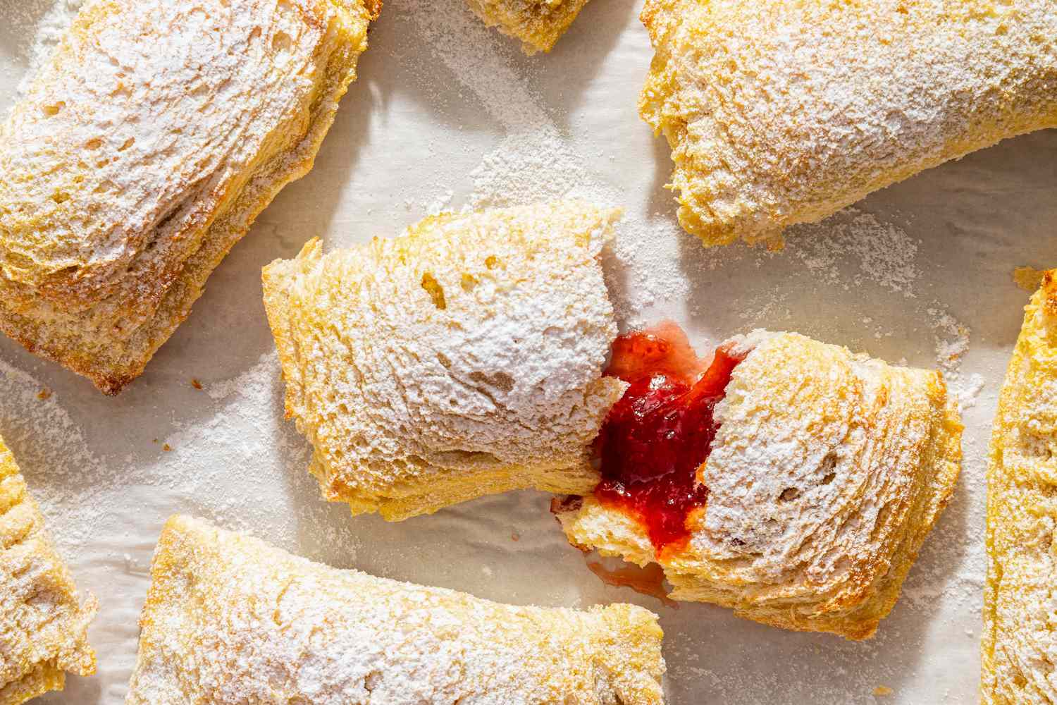 Toast Pies on a piece of parchment, dusted with powdered sugar, one torn open to show red filling