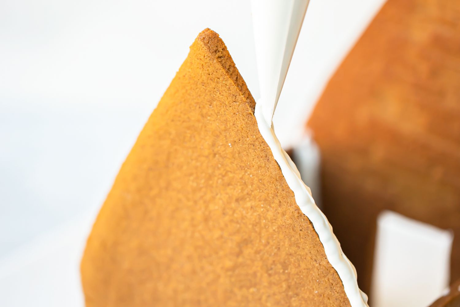 Piping royal icing on the sides to attach the roof to show how to make a gingerbread house.