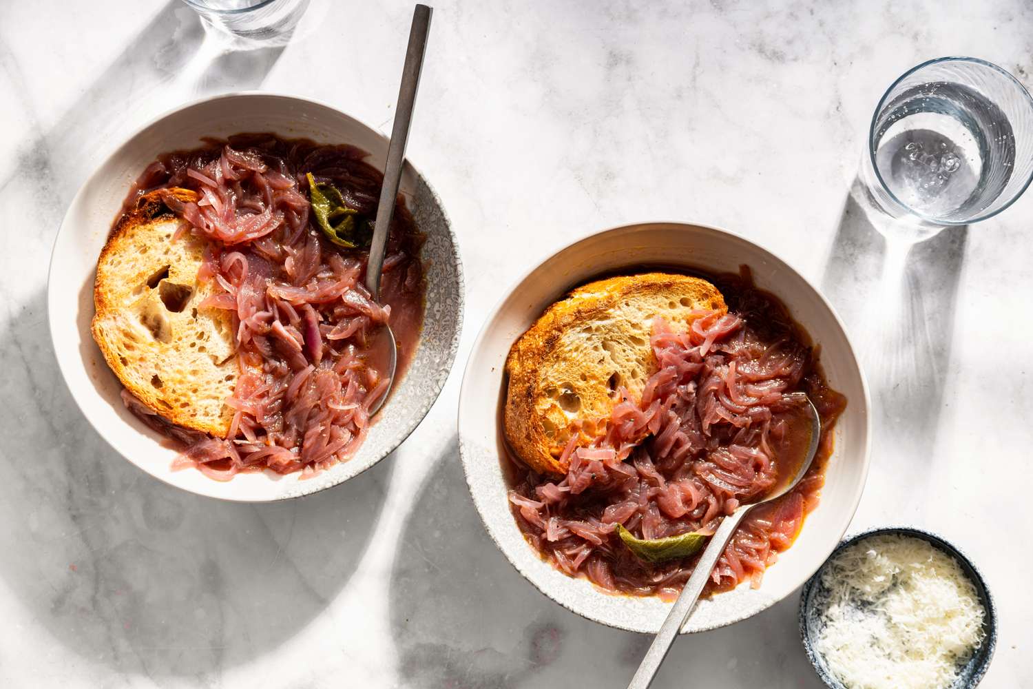 Two bowls of Tuscan onion soup with slices of bread and spoons viewed from above