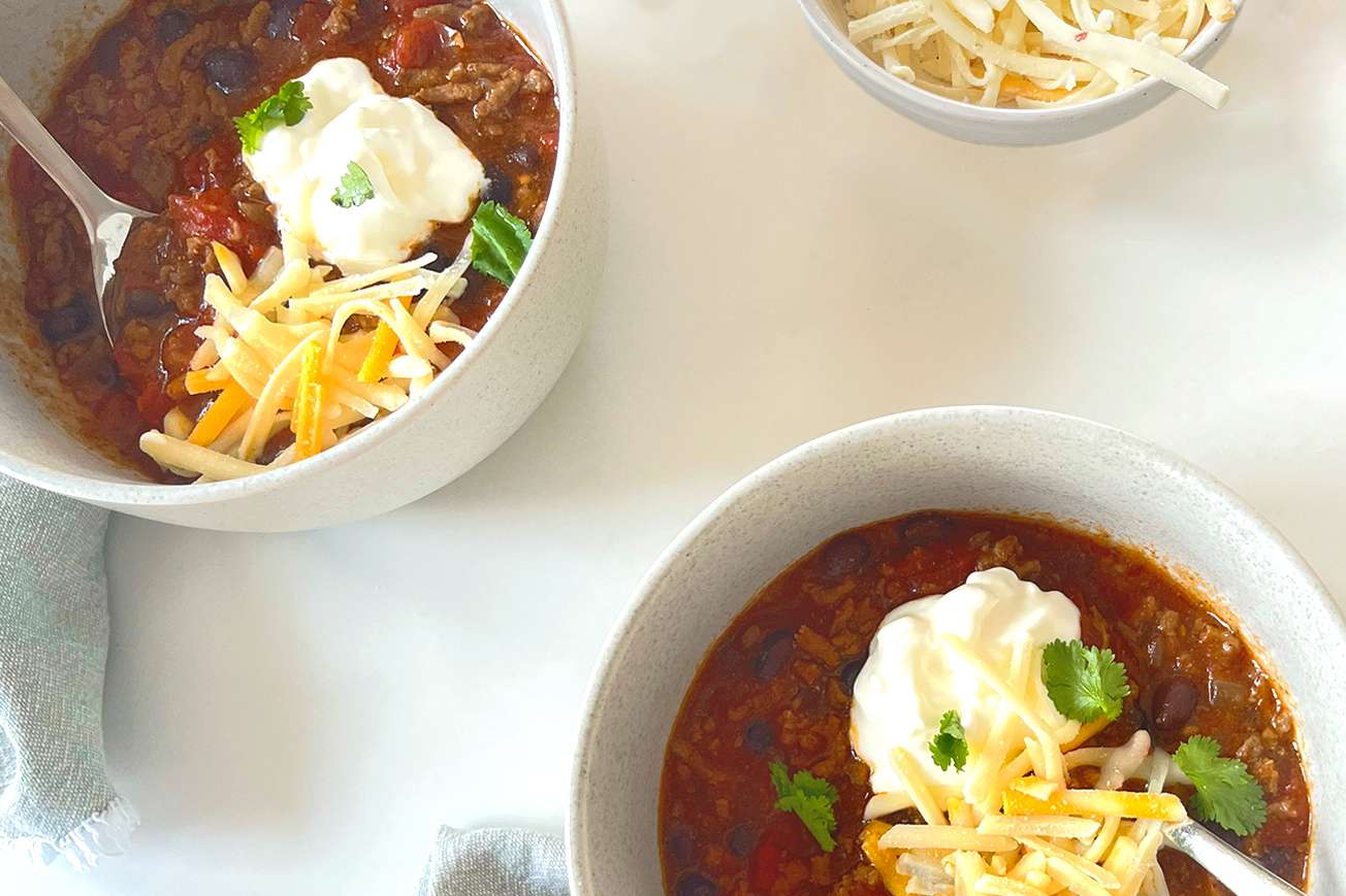Bowls of chili topped with shredded cheese sour cream and herbs served on a table