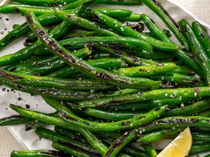 A closeup overhead shot of slightly charred pan fried green beans sprinkled with coarse salt and garnished with a lemon wedge