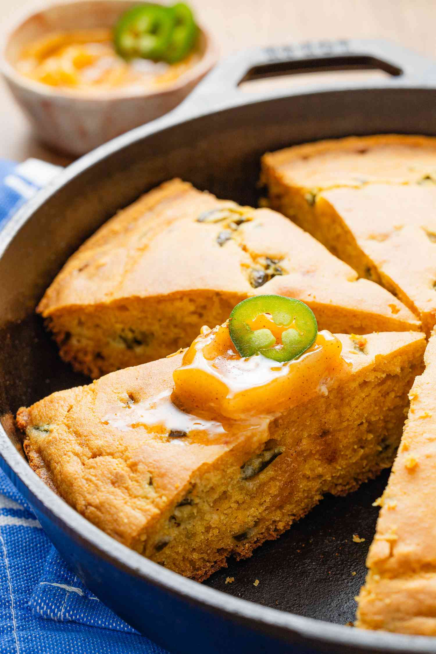 Hot honey cornbread (JalapeÃ±o Honey Cornbread) sliced in a cast iron skillet with one slice topped with hot honey butter