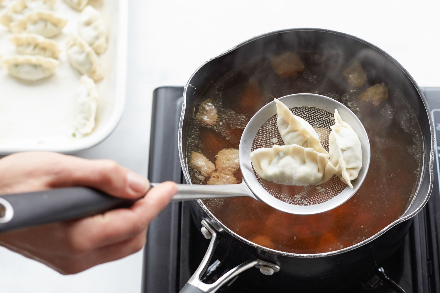 Adding mandu to a Korean dumpling beef soup in a pot on the stove.