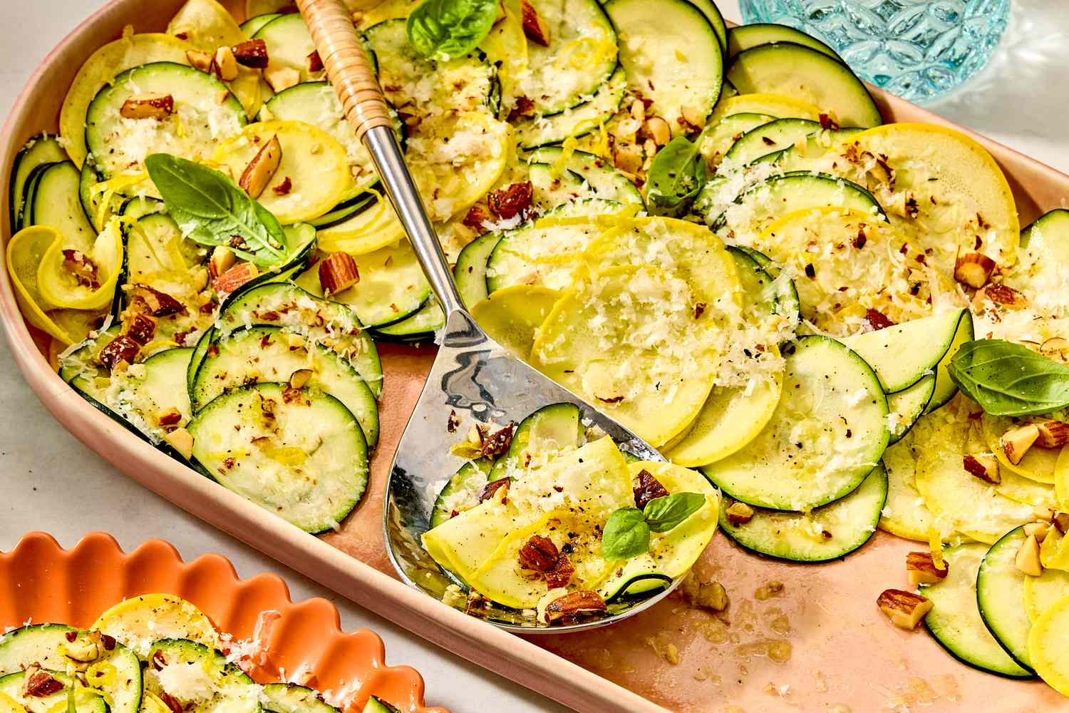A serving dish of thinly sliced summer squash salad topped with herbs and nuts