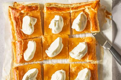 Lemon curd tart cut into squares, each topped with whipped cream.