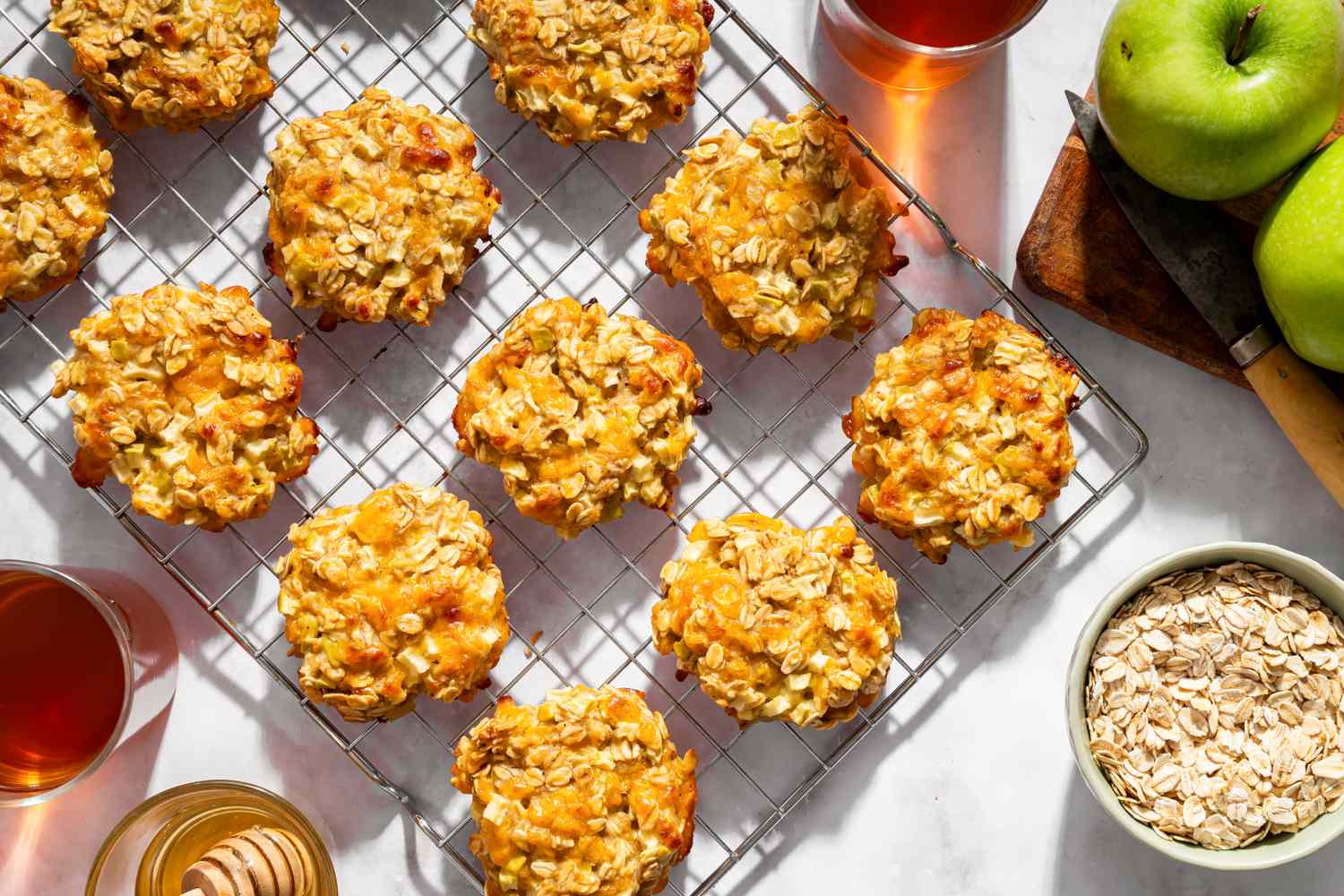 Apple oatmeal cookies placed on a cooling rack with green apples oats and beverages around