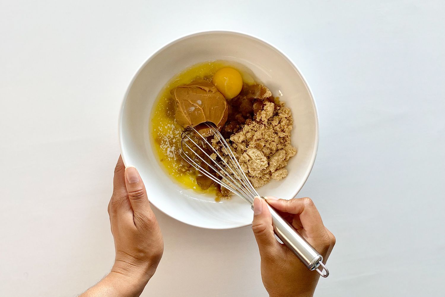 Whisking sugars and egg in a bowl to make Gluten-Free Sheet Pan Monster Cookies.