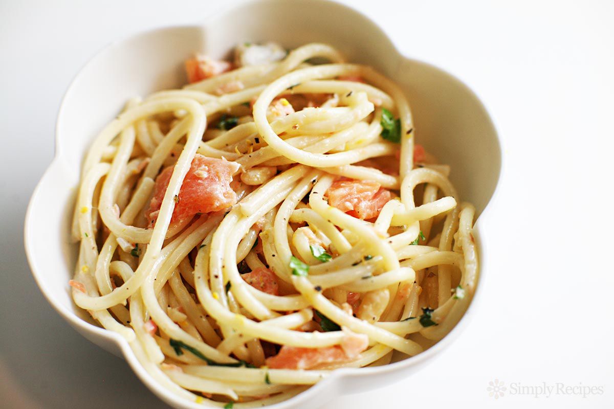 A dish of spaghetti pasta with pieces of smoked salmon and herbs in a scalloped bowl