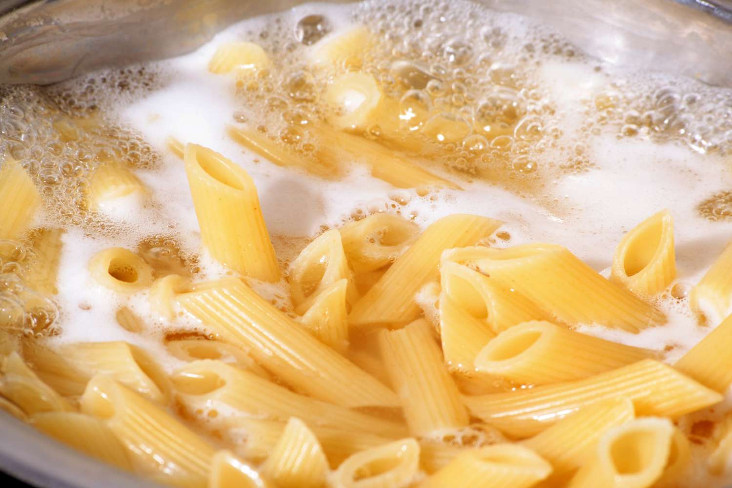 Penne pasta boiling in water with foam at the surface in a pot
