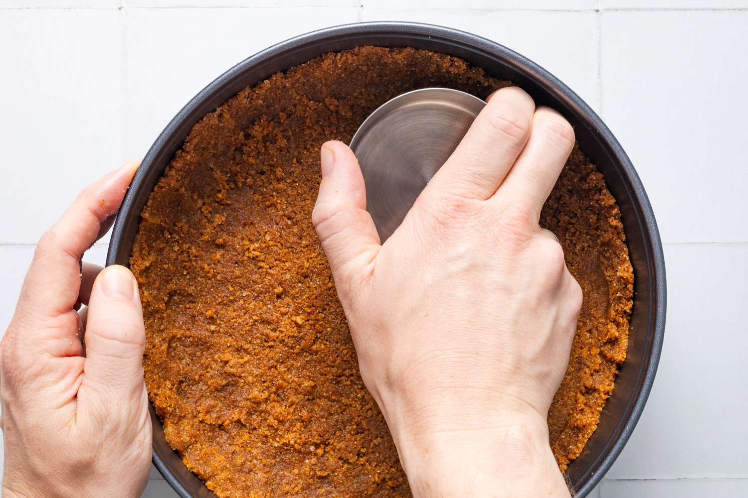 Bottom of measuring cup used to flatten and pack the cookie crumb layer in a springform pan for Cookie crumb, butter, and sugar blended together in a food processor for no-bake pumpkin cheesecake recipe