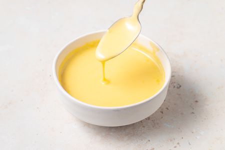 Blender Hollandaise Sauce in a white bowl with sauce dripping off of a spoon.