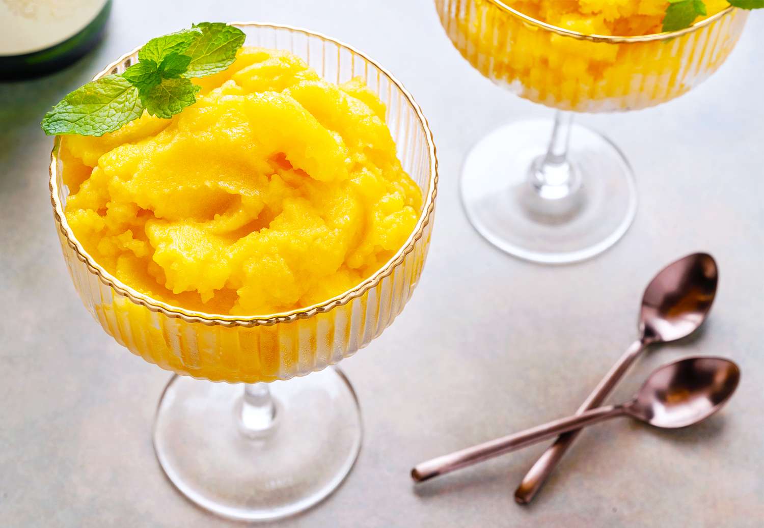 Two glass cups filled with a peach dessert and garnished with mint leaves accompanied by two spoons