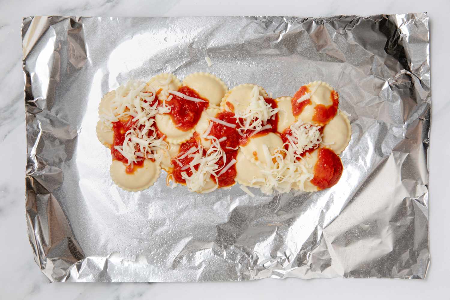 Ravioli topped with sauce and grated cheese on foil