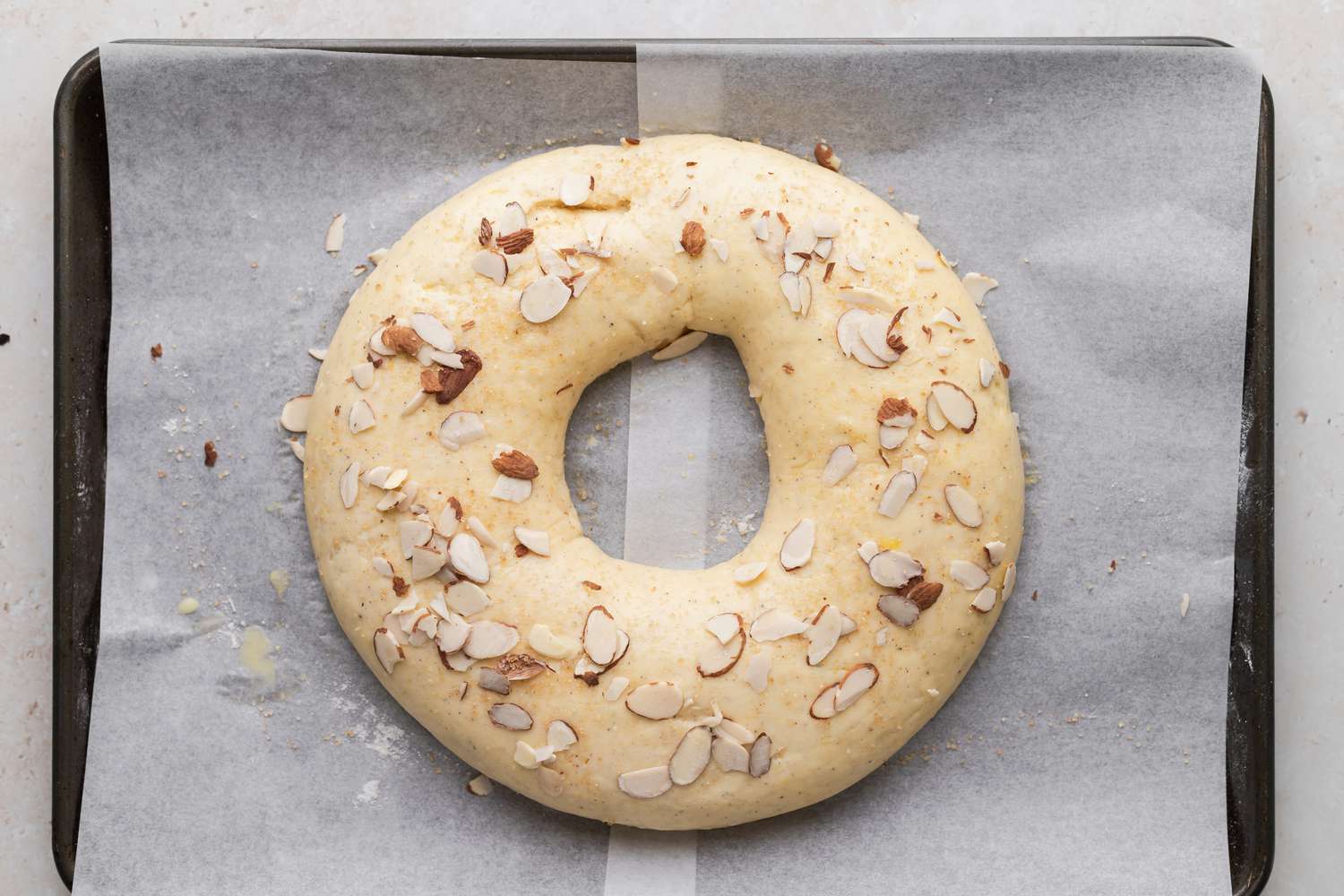 Overhead view of a kringle recipe topped with almonds on a parchment covered baking sheet.
