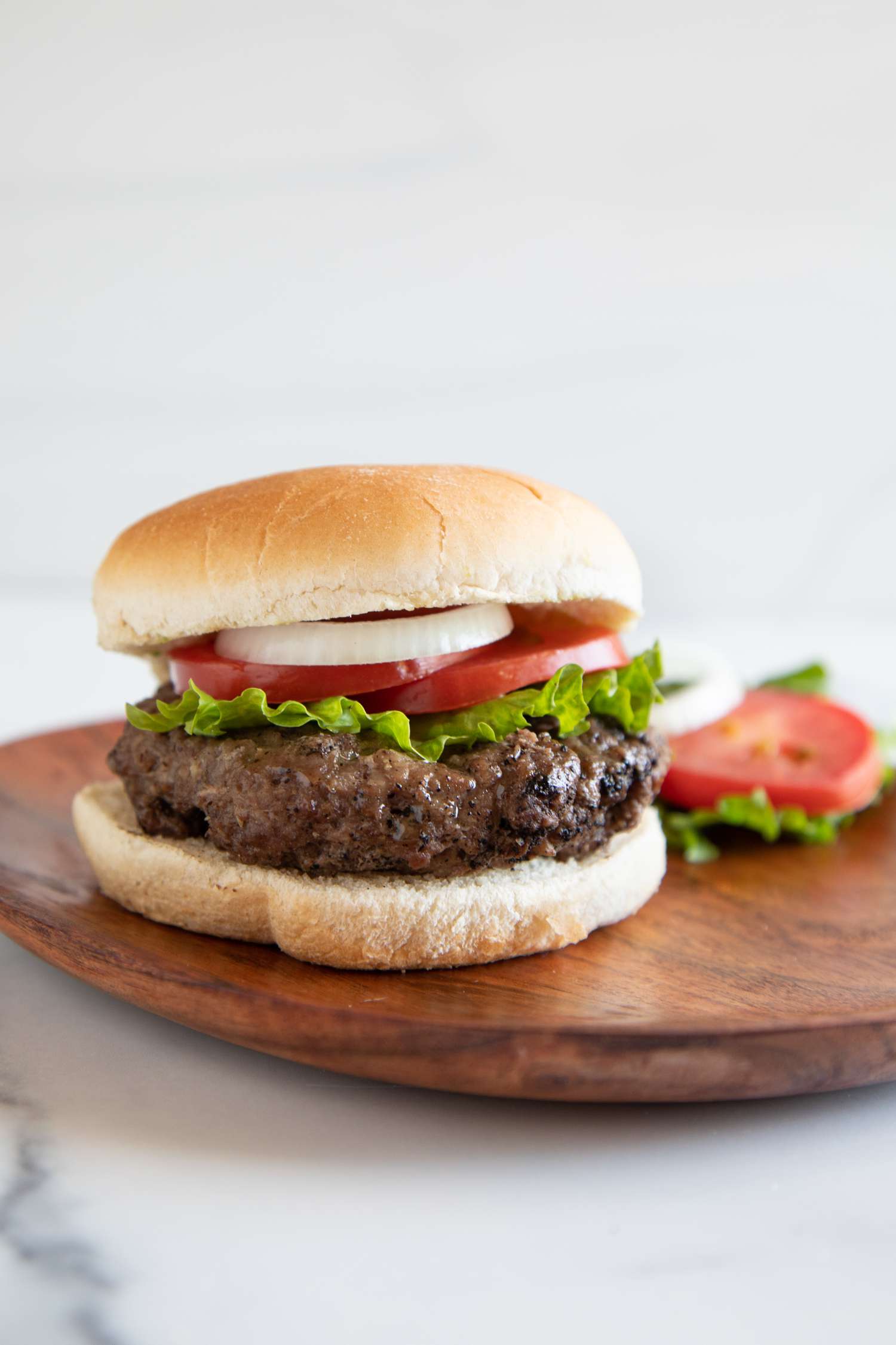 Hamburger with onion tomatoes and lettuce on a bun on a wooden plate