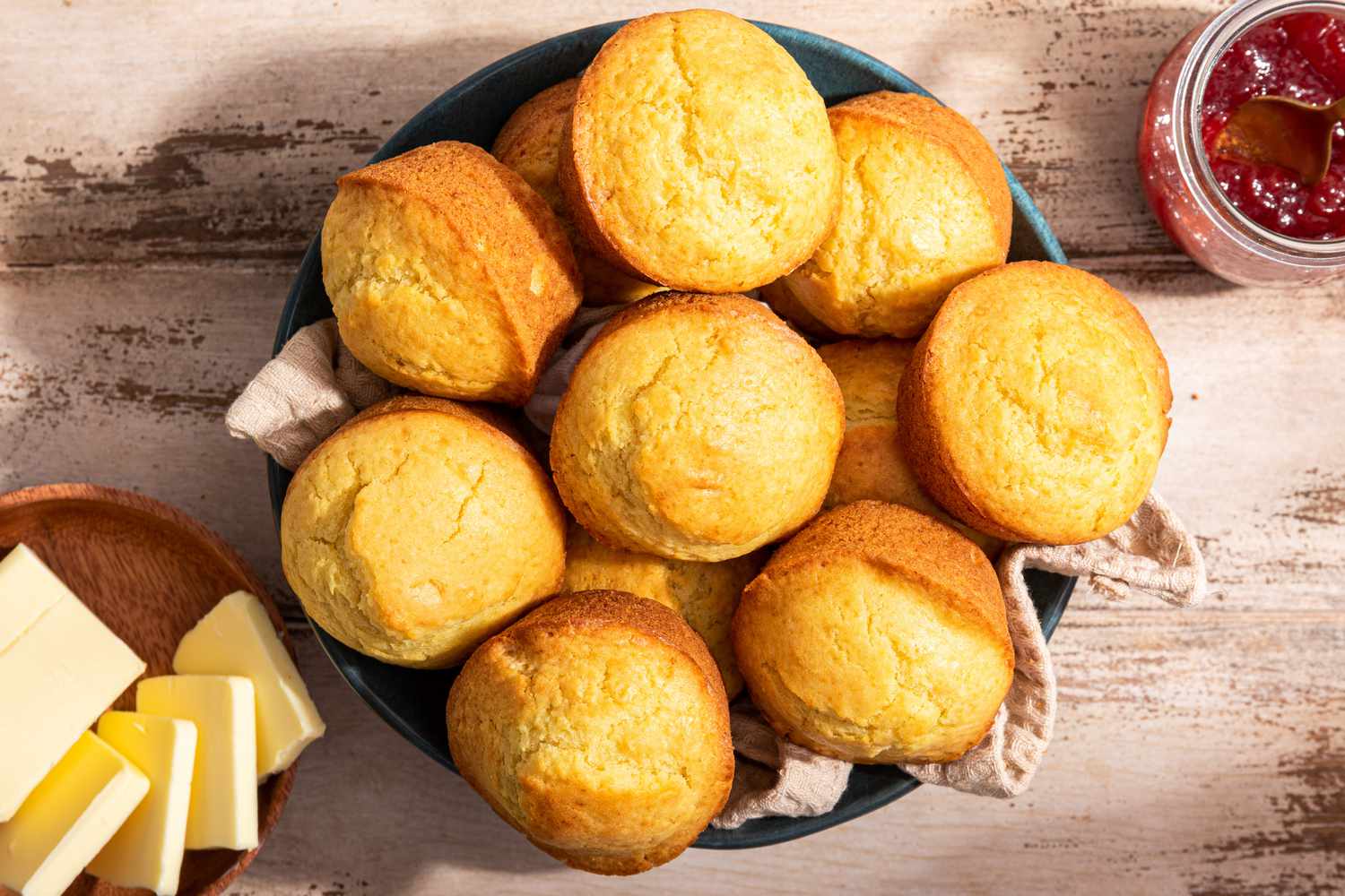 Nothin' muffins in a table napkin lined-bowl next to a bowl of butter and a jar of jam 