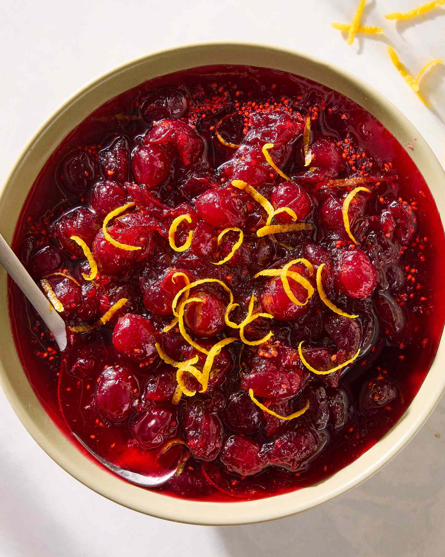 A bowl containing cranberry sauce garnished with orange zest