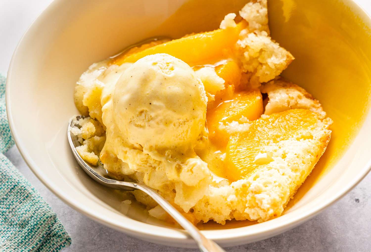 Bowl containing peach cobbler with a scoop of vanilla ice cream and a spoon