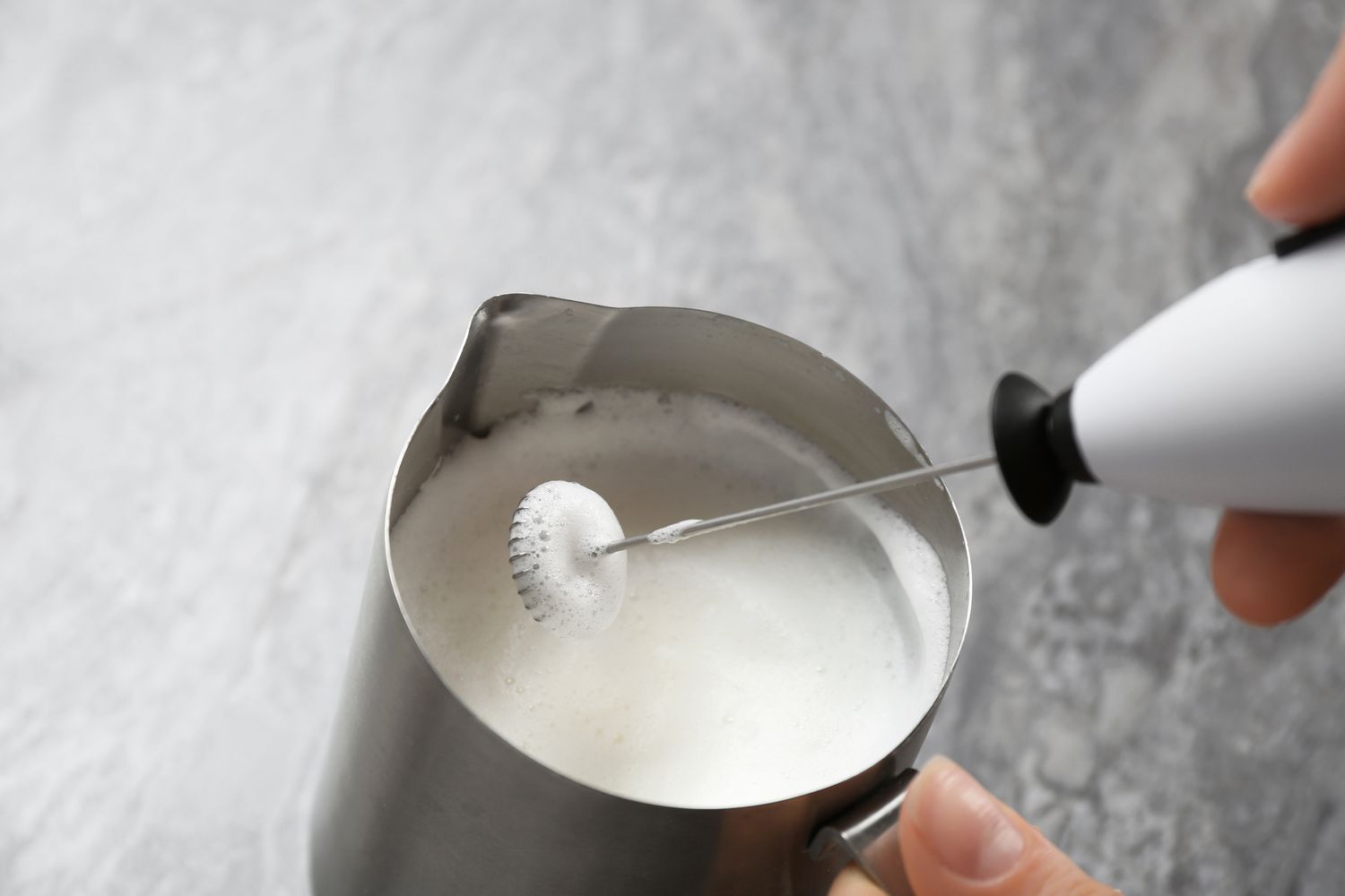 Closeup of woman using milk frother in pitcher on table