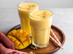 Two Glasses of Mango Lassi on Tray with Cubed Mango and Straws