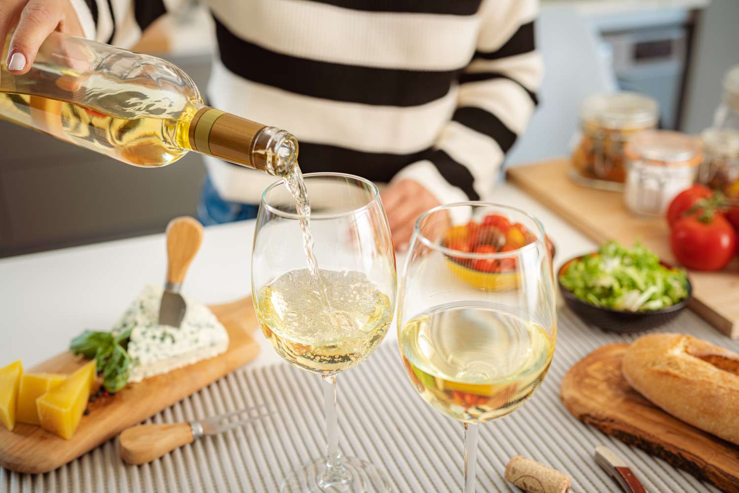 Someone wearing a striped shirt pouring white wine into stemmed wine glasses
