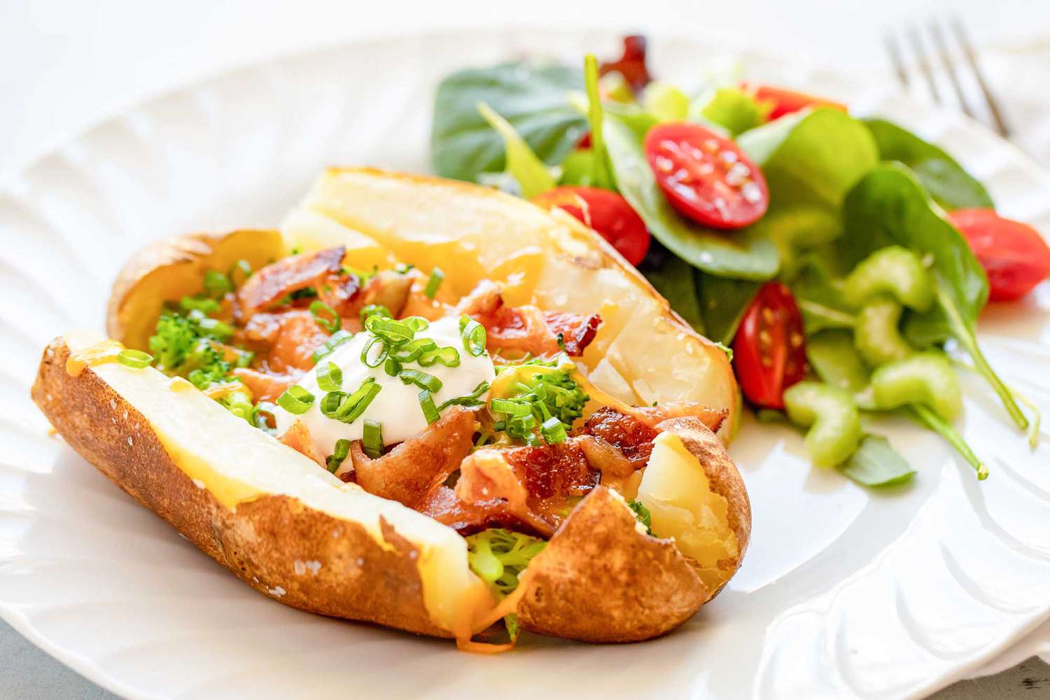 A loaded baked potato with salad on a plate ready to eat.