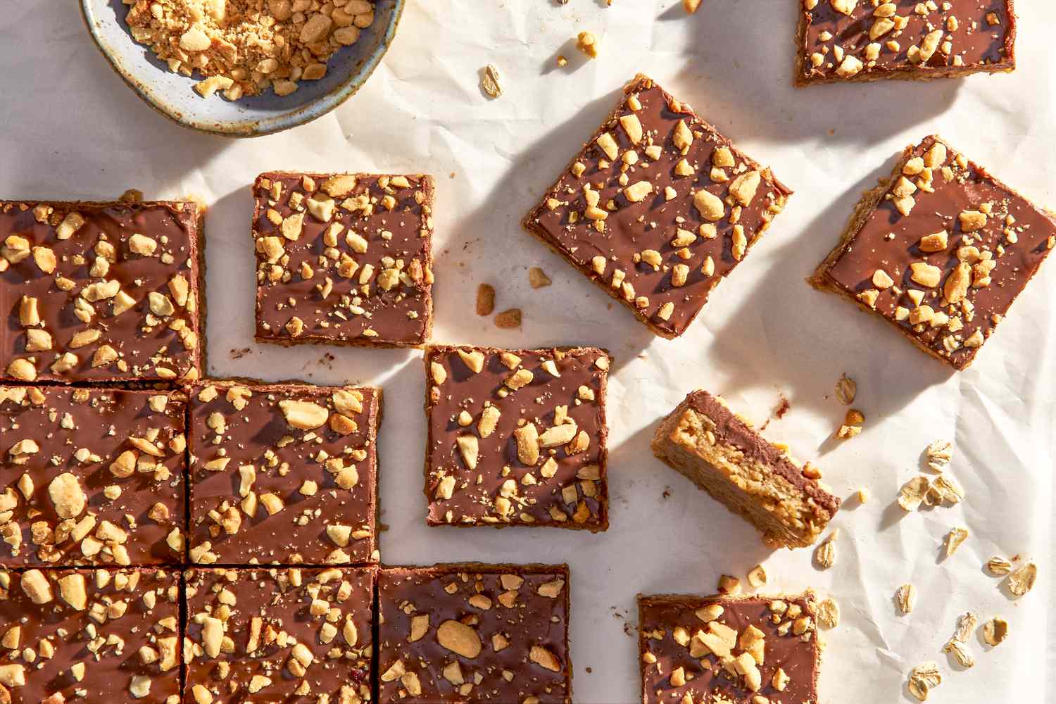 Oh Henry bars on a crinkled parchment paper with a bowl of crushed peanuts 