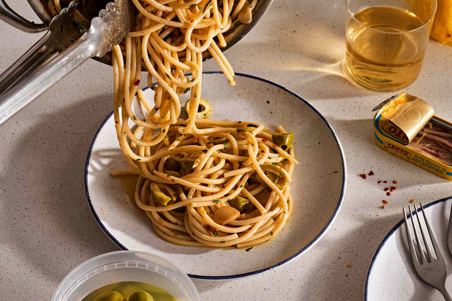 Pouring spaghetti aglio e olio from a skillet to a plate