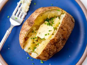 baked jacket potato cut open length wise and filled with butter and chives, on a blue pate with a fork on the left side