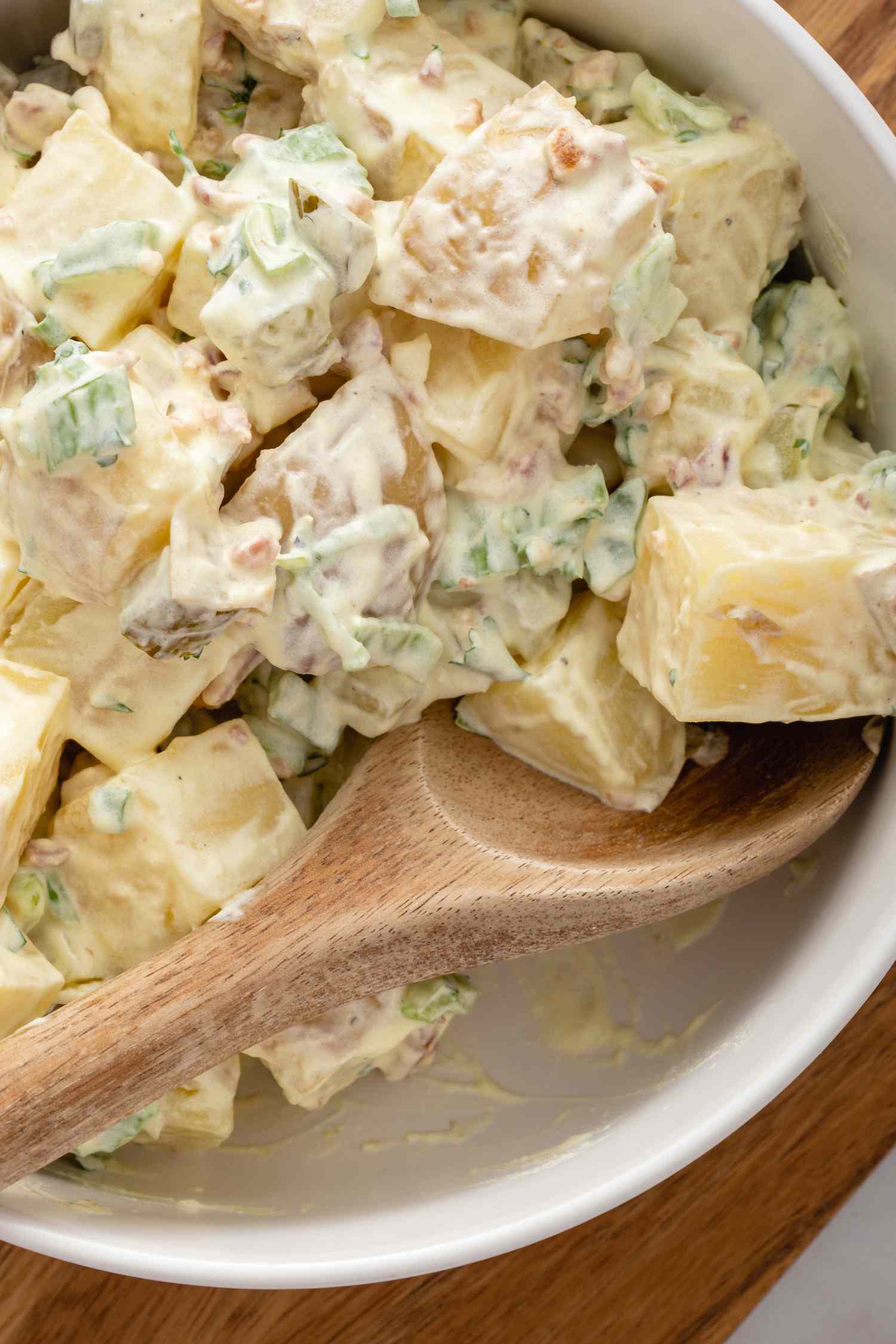 Close up overhead view of the best potato salad recipe in a white bowl with a spoon.