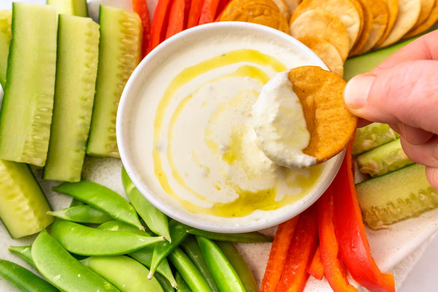 Platter of fresh vegetables and pita chips with a bowl of dipping sauce being used