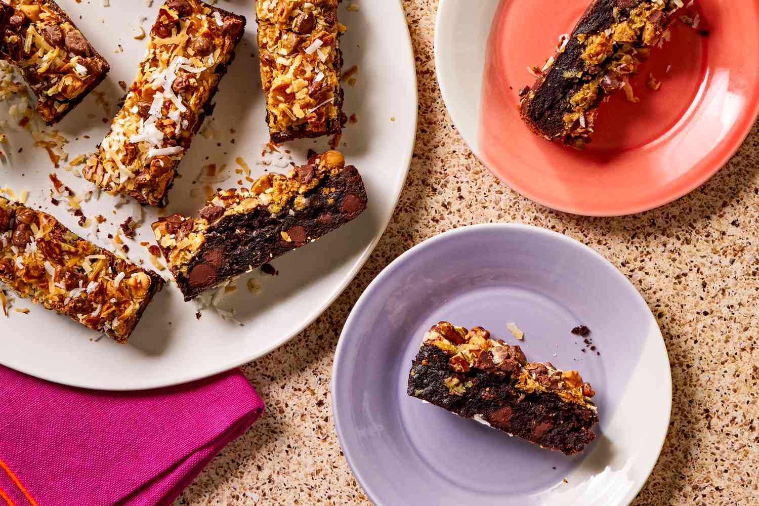 Overhead view of a white plate of hello dolly brownie bars next to two small plates with one bar all on a brown countertop